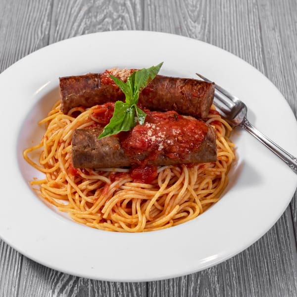 Spaghetti with two large sausages, marinara sauce, grated cheese, and basil on a white plate.