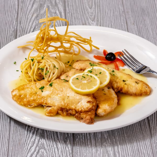 Tony Sopranos' chicken piccata with spaghetti, lemon slices, and a decorative garnish on a white plate.