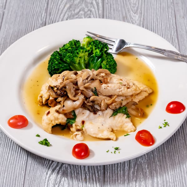 Chicken with mushrooms, broccoli, and cherry tomatoes in a sauce on a white plate with a fork.