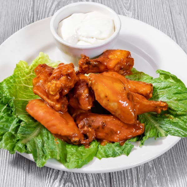 Tony Sopranos Pizza & Ristorante's buffalo wings with ranch dressing and lettuce on a white plate.