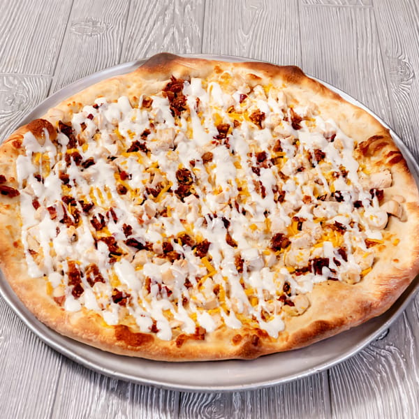 Tony Sopranos Pizza with chicken, bacon, cheese, and white sauce on a metal pan.