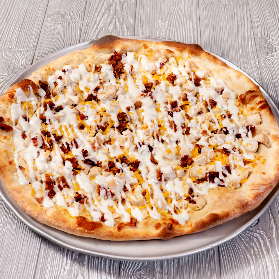 Tony Sopranos Pizza with chicken, bacon, cheese, and white sauce on a metal pan.